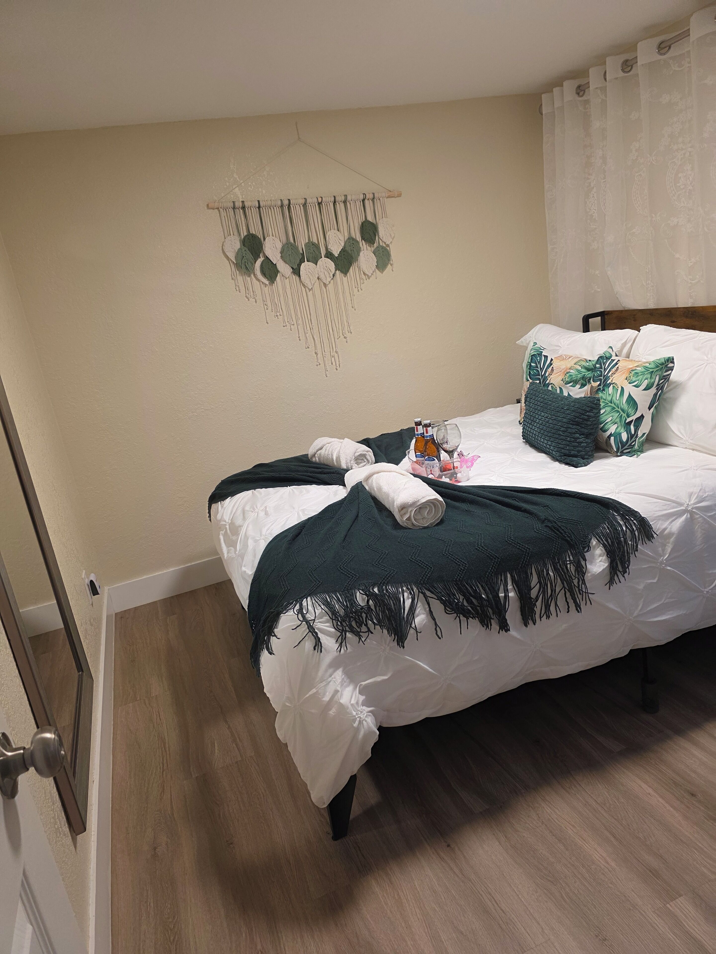A neatly made bed with white linens, a dark green throw blanket, and tropical-themed pillows.