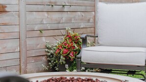 A round table with a white cushion, a wooden fence, and a chair with a white cushion. - Gas Fire Pit/Coffee Bar/Walk to Downtown/EV/Pets/AC (Enumclaw)