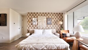 A bedroom with a large bed, a wooden floor, a checkered wall, and a window with blinds. - Gas Fire Pit/Coffee Bar/Walk to Downtown/EV/Pets/AC (Enumclaw)
