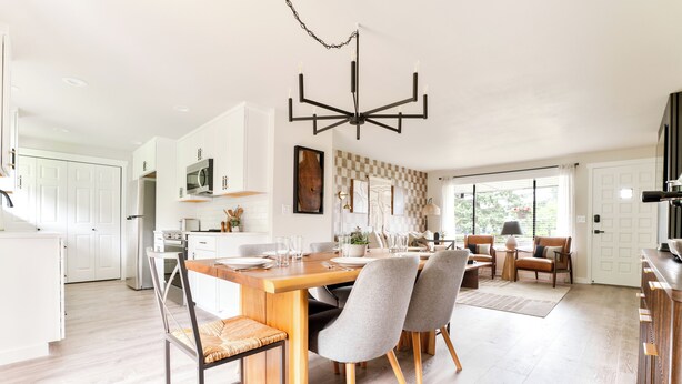 A modern kitchen with white cabinets, a wooden dining table, and a chandelier. - Gas Fire Pit/Coffee Bar/Walk to Downtown/EV/Pets/AC (Enumclaw)