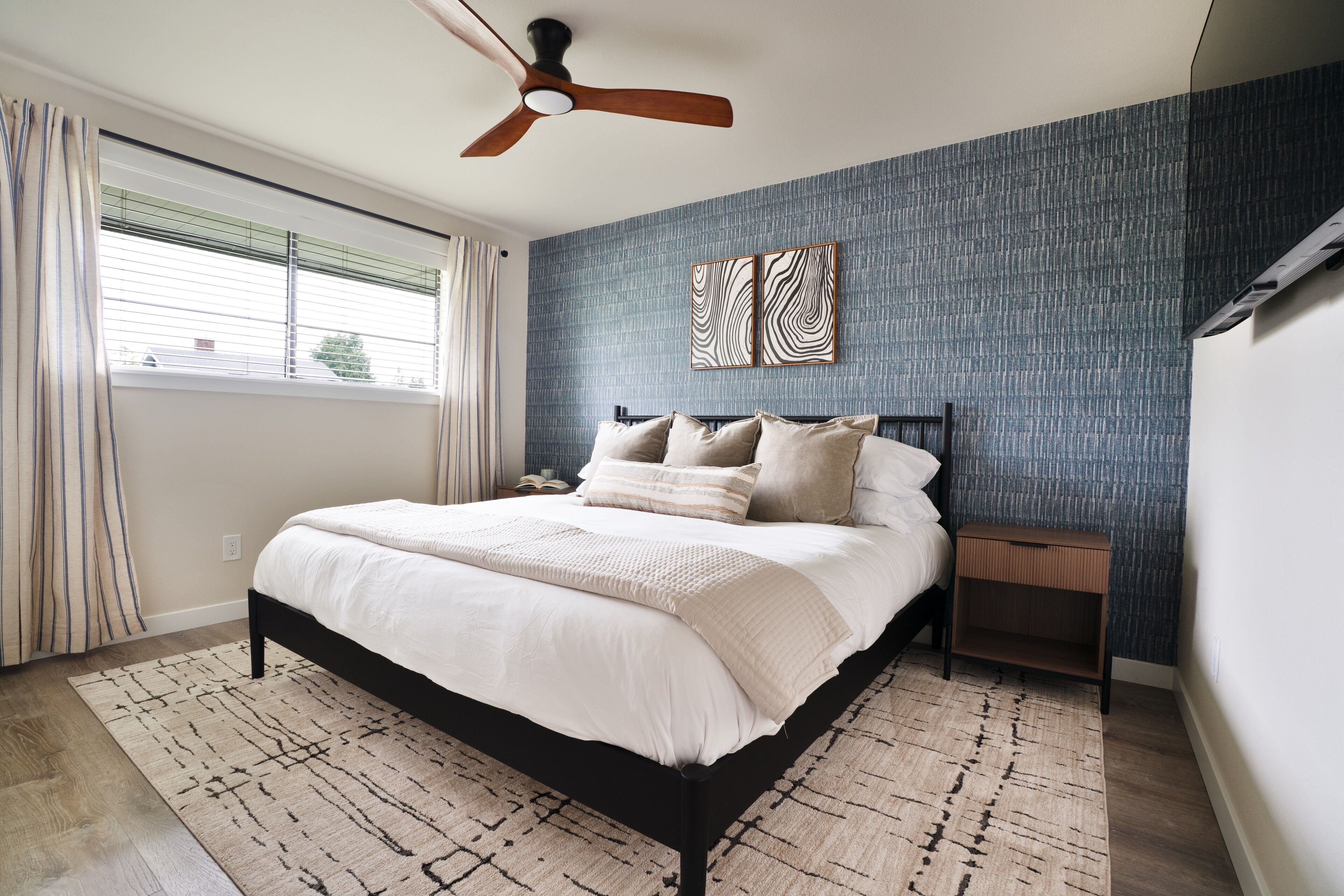 A bedroom with a bed, a nightstand, a ceiling fan, and a window with curtains.