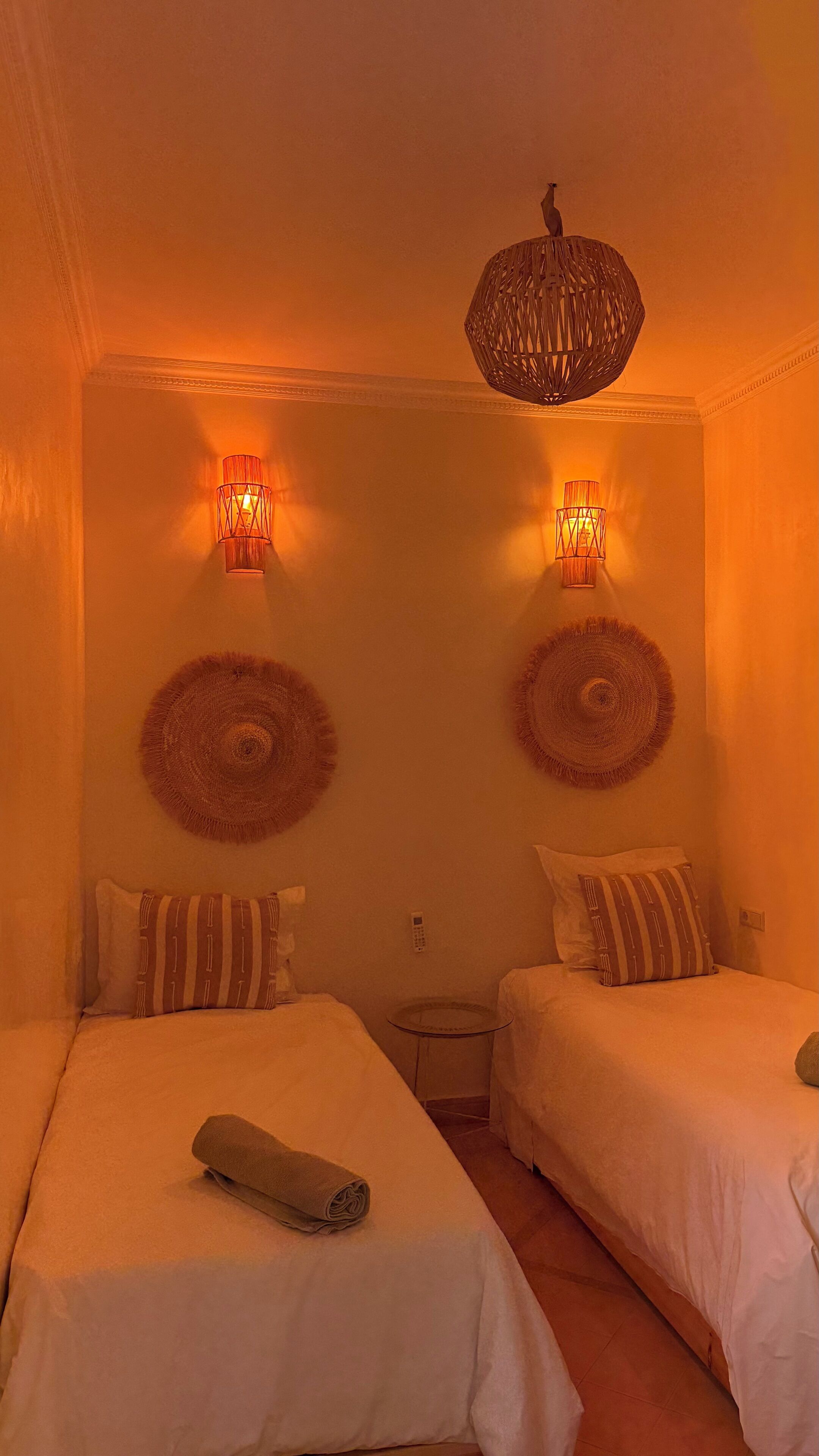 Una habitación con dos camas, una mesita pequeña, un teléfono en la pared y una lámpara decorativa colgante.