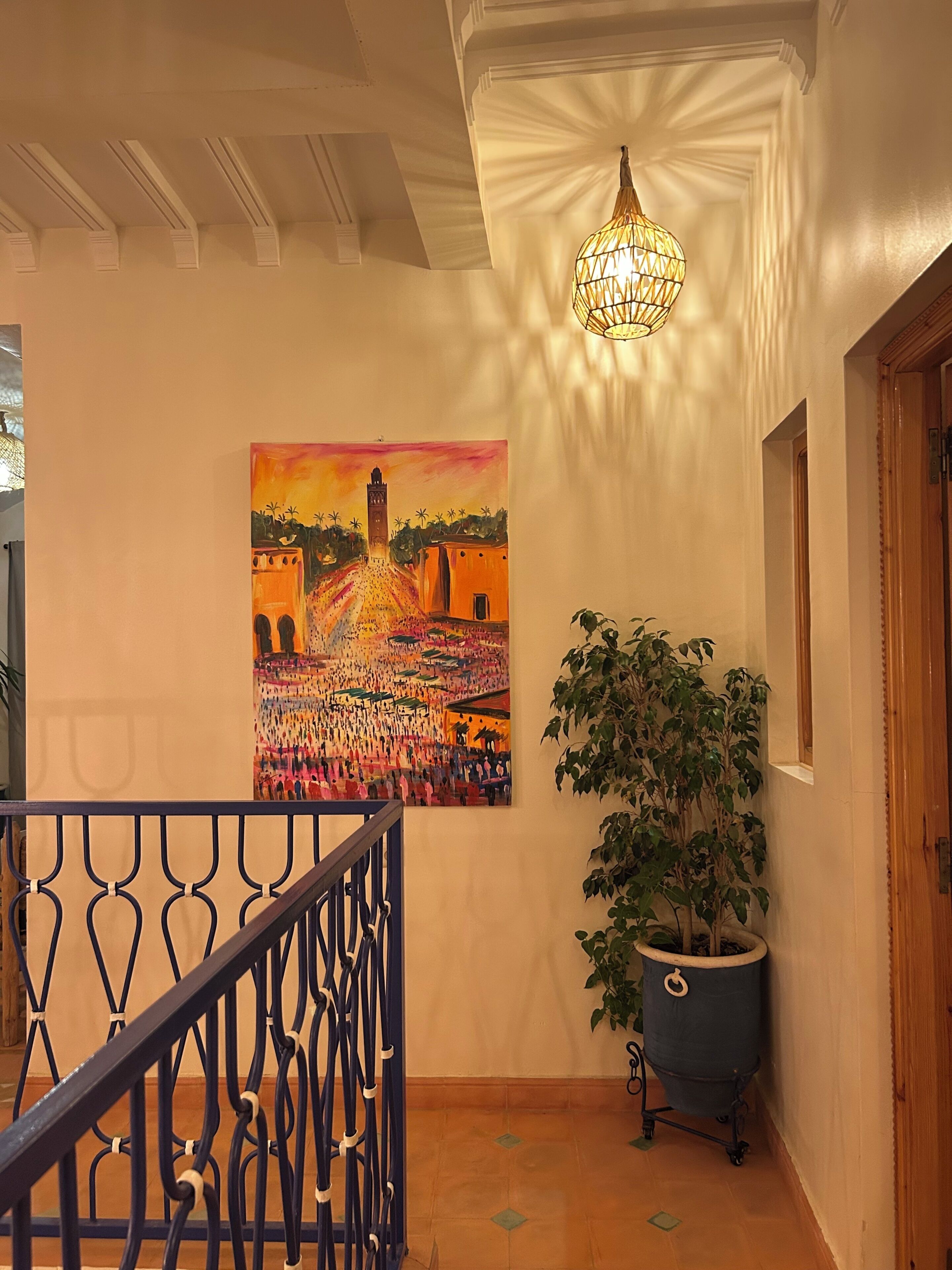 Ein Flur mit Treppe, einem Gemälde, einem Topfpflanzen und einer Chandelier.