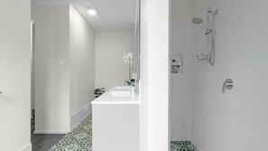 A modern bathroom with a white sink, a shower with a handheld showerhead, and a small shelf with toiletries. - Bikinis & Martinis - Jervis Bay (Vincentia)
