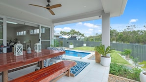 A covered patio with a pool, wooden furniture, and a view of the backyard. - Bikinis & Martinis - Jervis Bay (Vincentia)