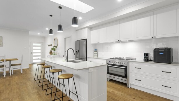 A modern kitchen with white cabinetry, a central island with stools, a stainless steel refrigerator, a gas stove, and a coffee machine. - Bikinis & Martinis - Jervis Bay (Vincentia)