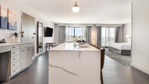 Habitación de hotel moderna con una isla de mármol, una cama, zona de comedor y vistas a la ciudad.