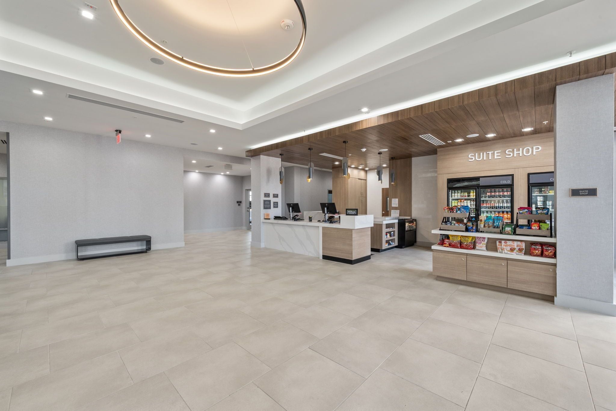 A modern hotel lobby with a reception desk, a 'Suite Shop' with snacks, and a clean, minimalist design.