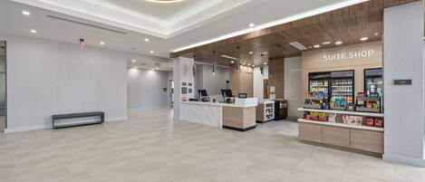 A modern hotel lobby with a reception desk, a 'Suite Shop' with snacks, and a clean, minimalist design.