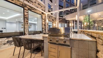 An outdoor kitchen area with a built-in grill, seating, and a stone wall backdrop.