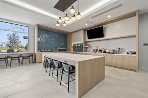 Een moderne keuken met een centraal eiland, barkrukken, een flatscreen televisie en een groot raam met uitzicht op een aangelegde tuin.