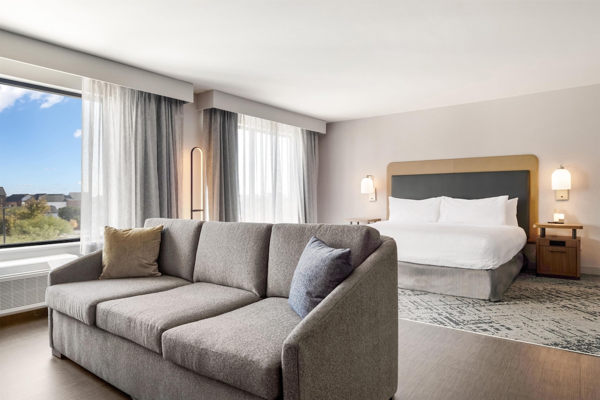 Een hotelkamer met een slaapbank, een bed, een nachtkastje en uitzicht op het groen.