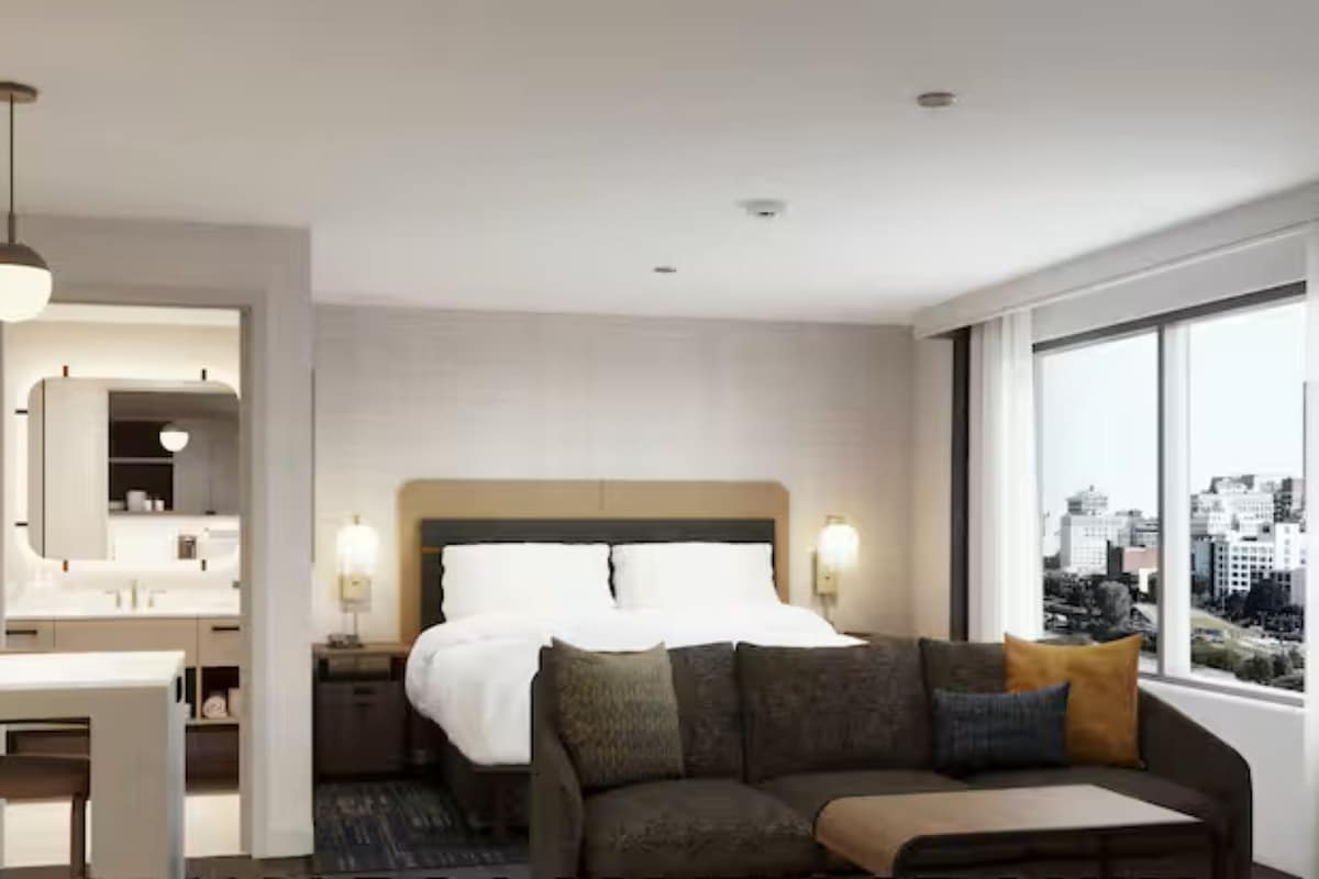 Une chambre d’hôtel comprenant un lit, un canapé, une table à manger et une grande fenêtre donnant sur la ville.