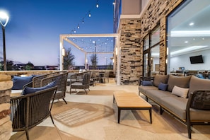 An outdoor patio area with wicker furniture, a stone wall, and string lights. - Homewood Suites By Hilton Austin Airport (Austin)