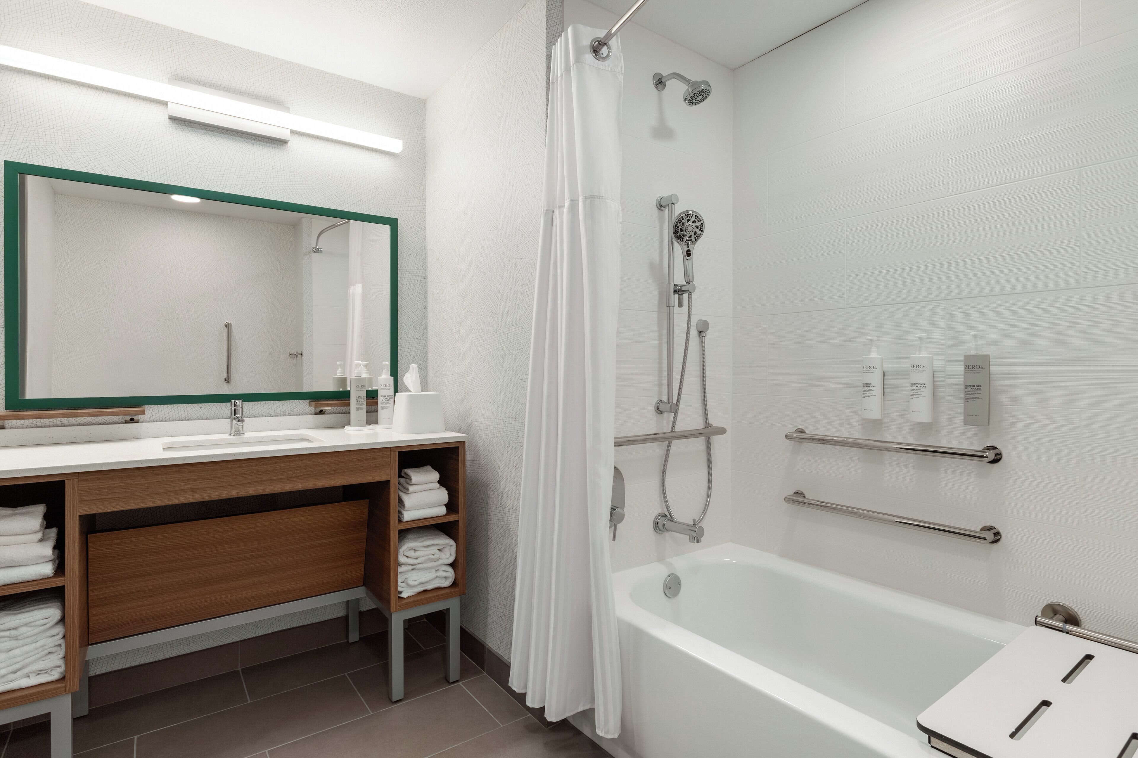 A modern bathroom with a white bathtub, a shower with a glass door, a wooden vanity with a mirror, and a towel rack.