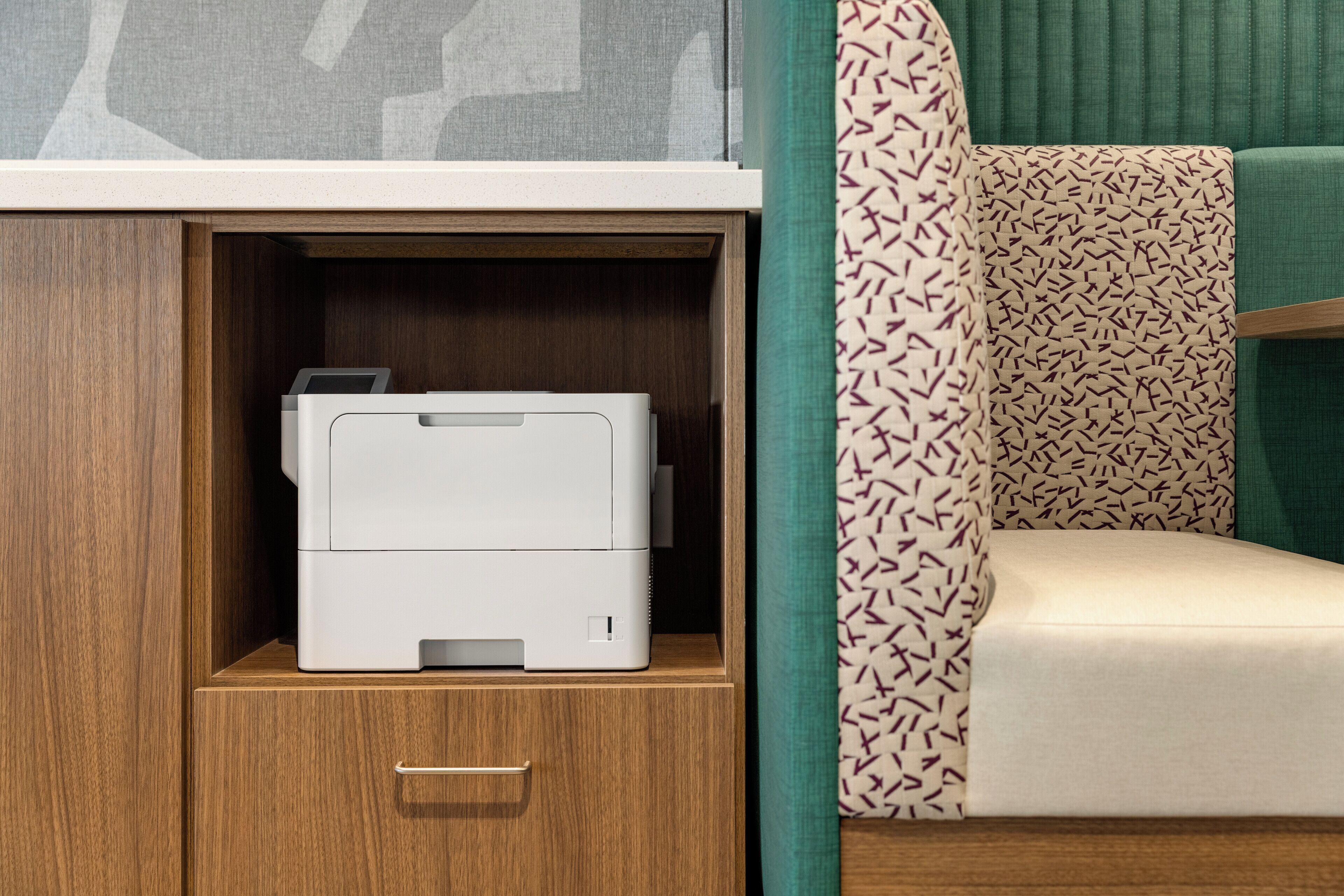 A printer in a wooden cabinet, a patterned pillow, and a green curtain.