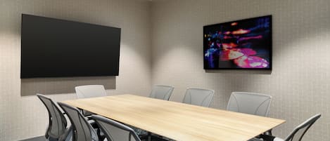 Un salón de conferencias con una larga mesa, seis sillas, un televisor de pantalla plana grande y un cuadro abstracto colorido en la pared.