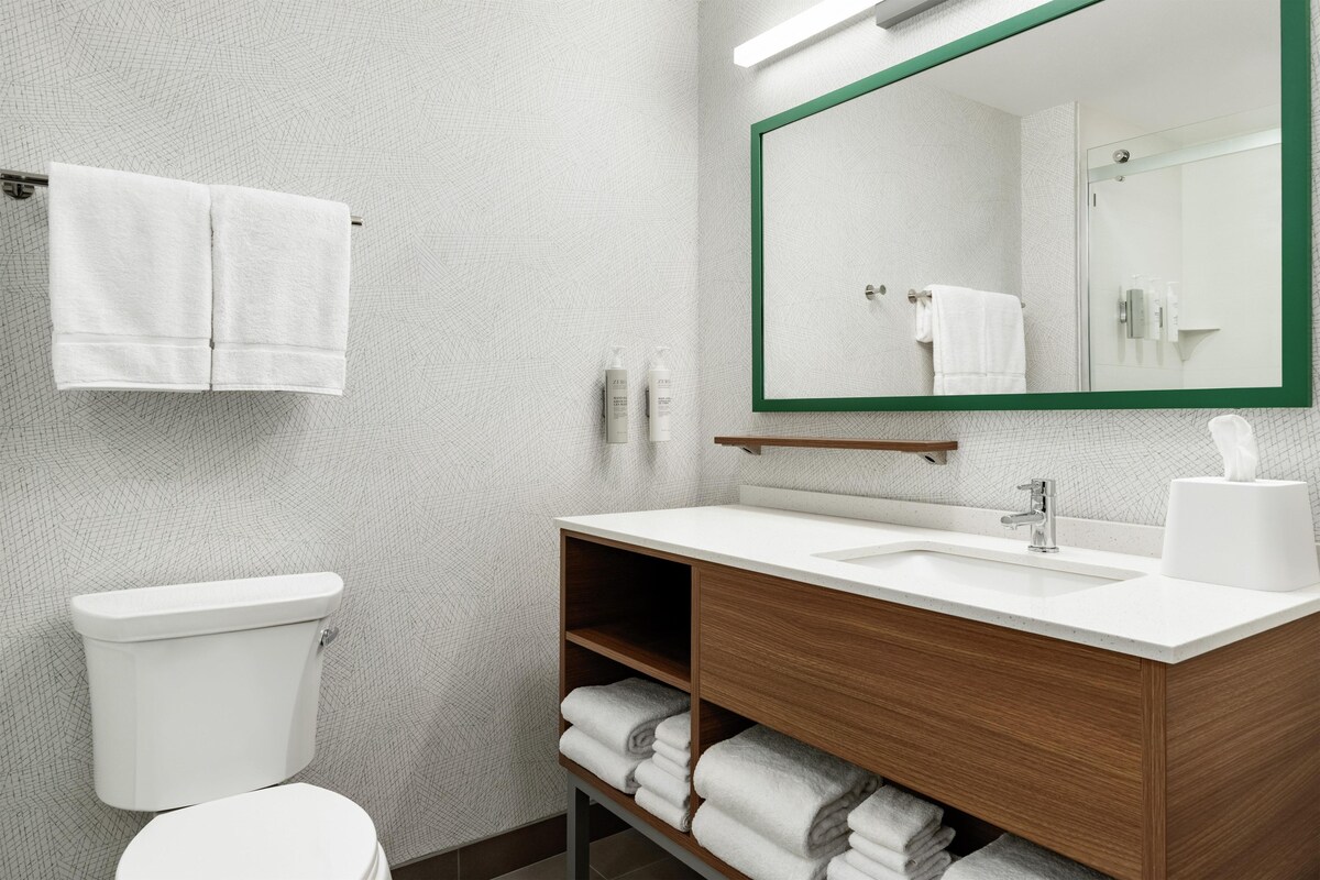 Ein modernes Badezimmer mit einer weißen Toilette, einem Holzwaschtisch mit Waschbecken und einem großen Spiegel mit grünem Rahmen.