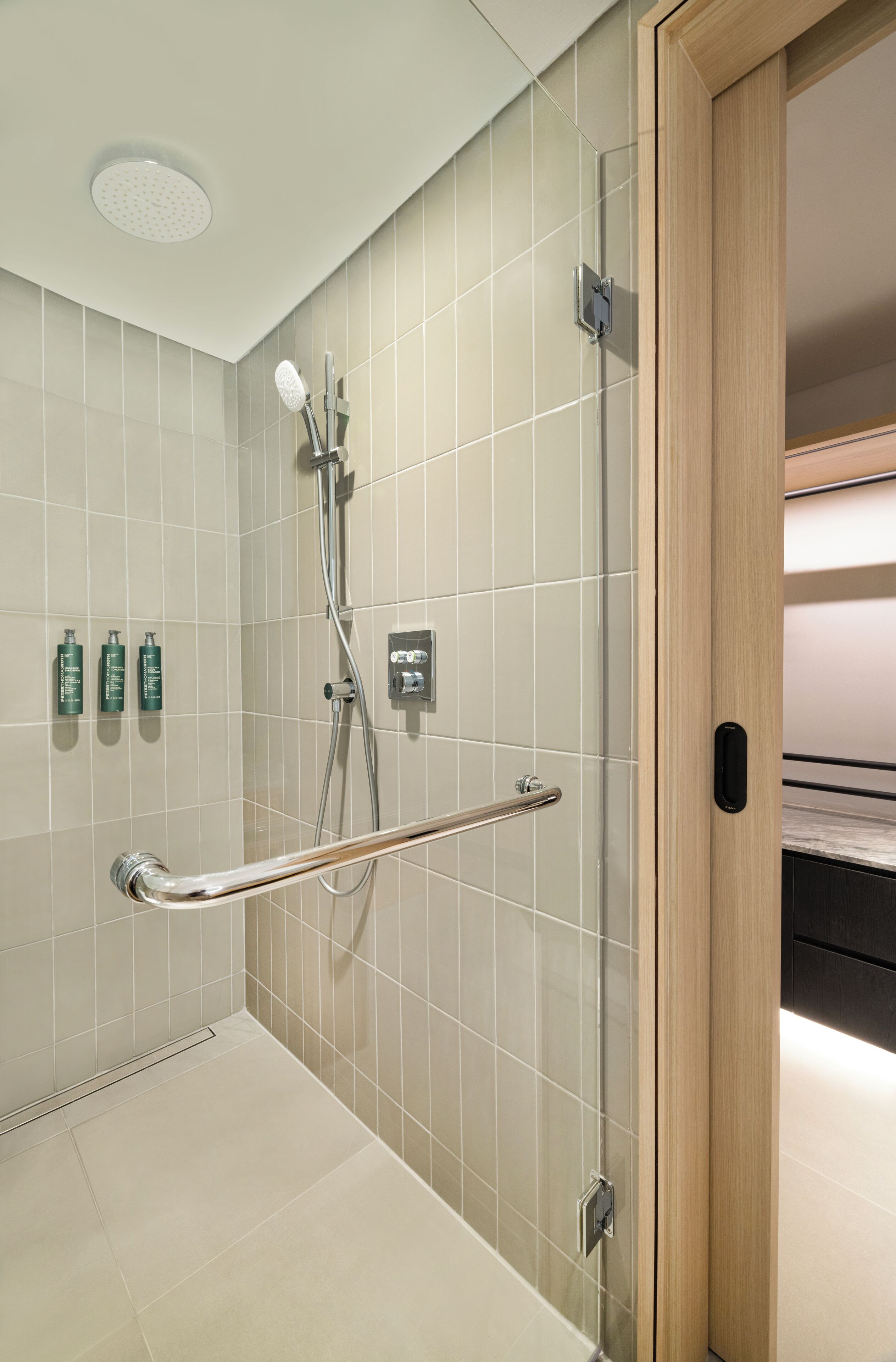 A modern bathroom with a shower, grab bar, and three green bottles on the wall.