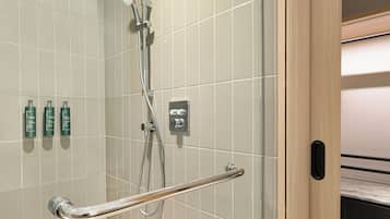 A modern bathroom with a shower, grab bar, and three green bottles on the wall.
