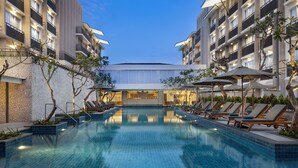A modern hotel with a swimming pool, sun loungers, and a well-lit entrance. - Hilton Garden Inn Bali Nusa Dua (Nusa Dua)