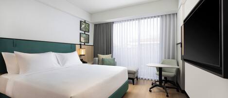 A hotel room with a large bed, a desk, a chair, and a TV.