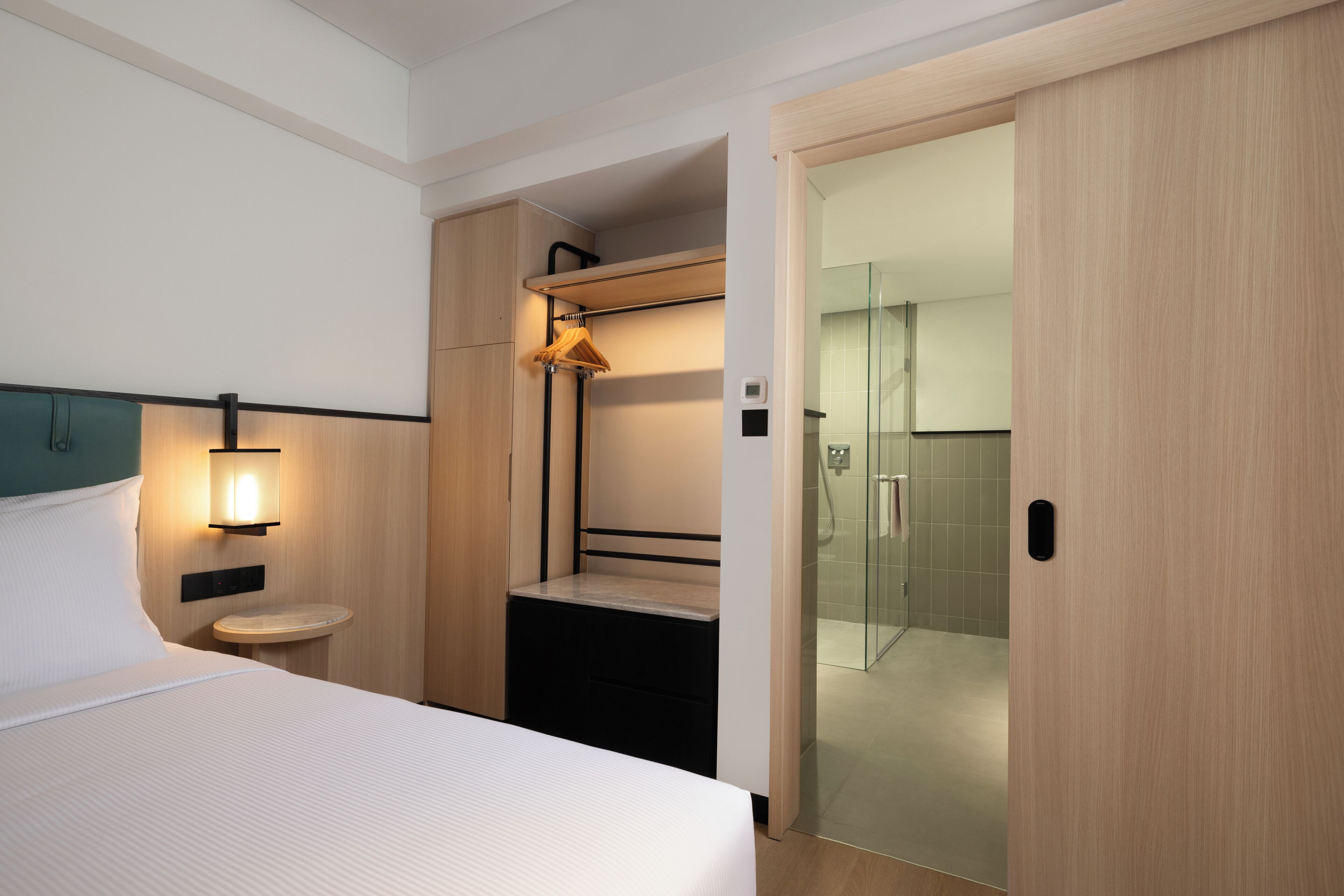 A hotel room with a bed, bedside table, and a glass-enclosed shower area.