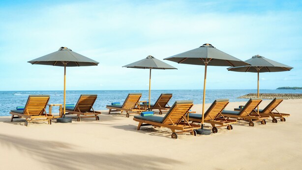 A beach with wooden lounge chairs and umbrellas. - Hilton Garden Inn Bali Nusa Dua (Nusa Dua)