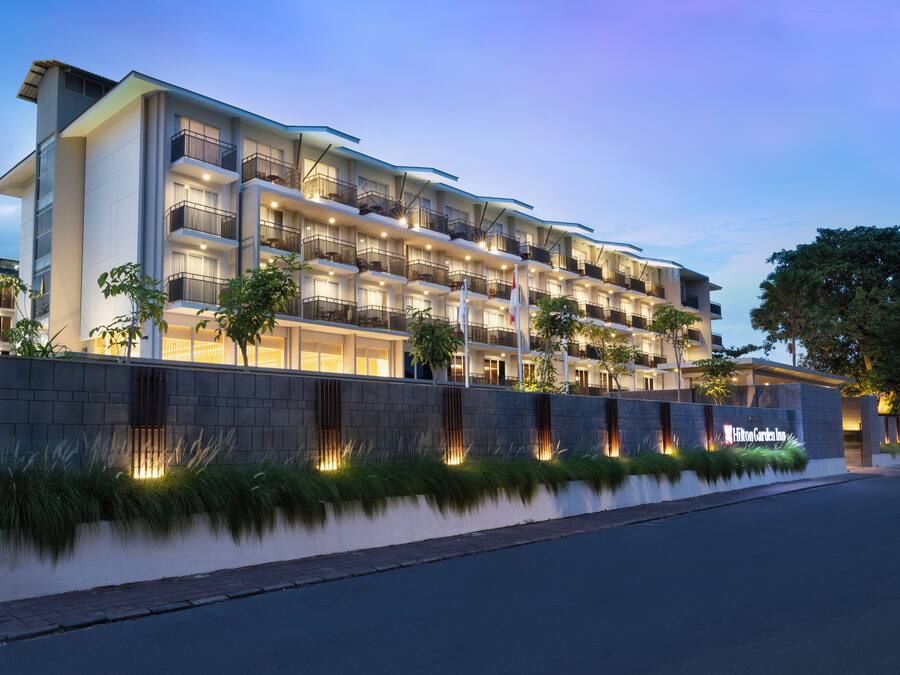 A multi-story hotel with balconies, a well-lit facade, and a landscaped front.