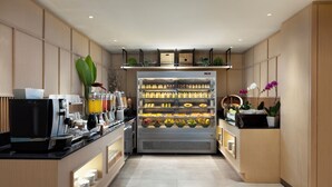 A modern kitchen with a coffee machine, a refrigerated display case with various food items, and a counter with a coffee station. - Hilton Garden Inn Bali Nusa Dua (Nusa Dua)