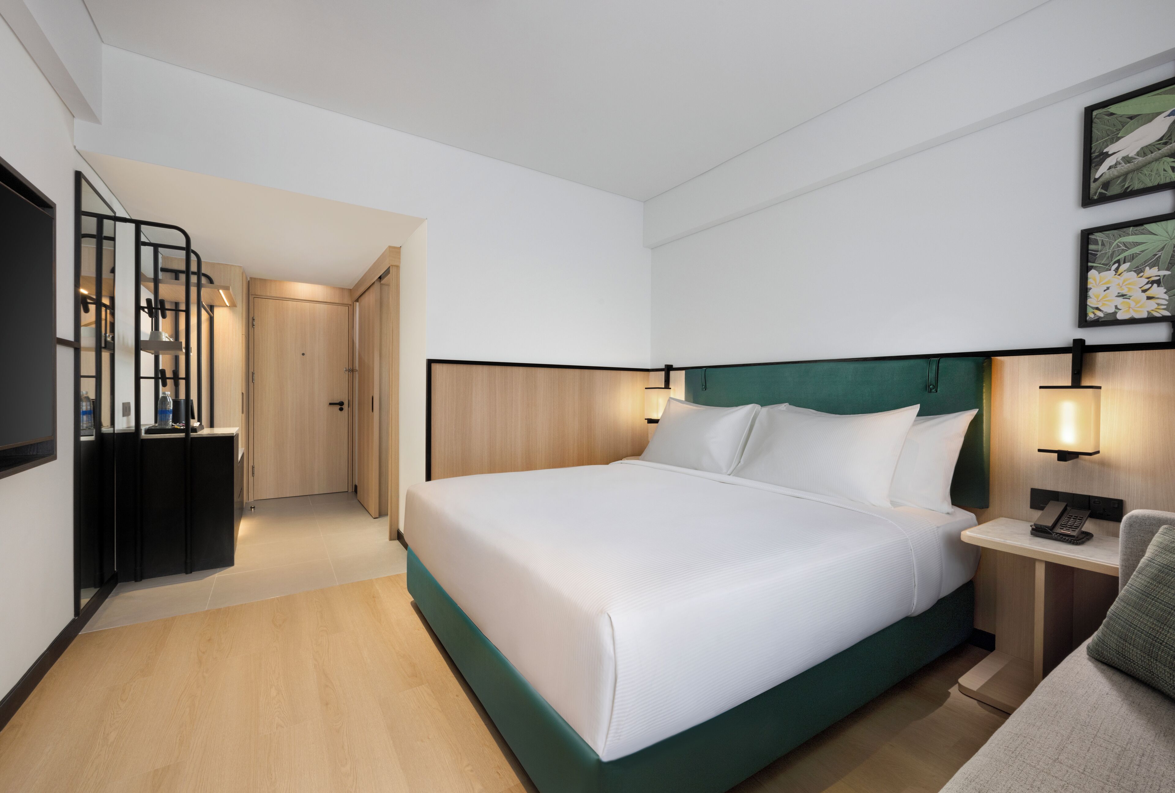 A modern hotel room with a large bed, a desk with a lamp, and a television.