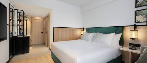 A modern hotel room with a large bed, a desk with a lamp, and a television.