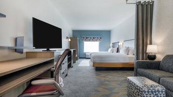 A hotel room with a bed, a desk with a flat-screen TV, a chair, a sofa, and a patterned carpet.
