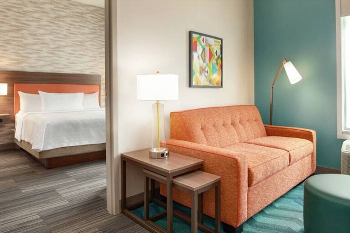 Une chambre d’hôtel avec un lit, un canapé, une table de chevet avec une lampe et un tableau abstrait aux couleurs vives accroché au mur.