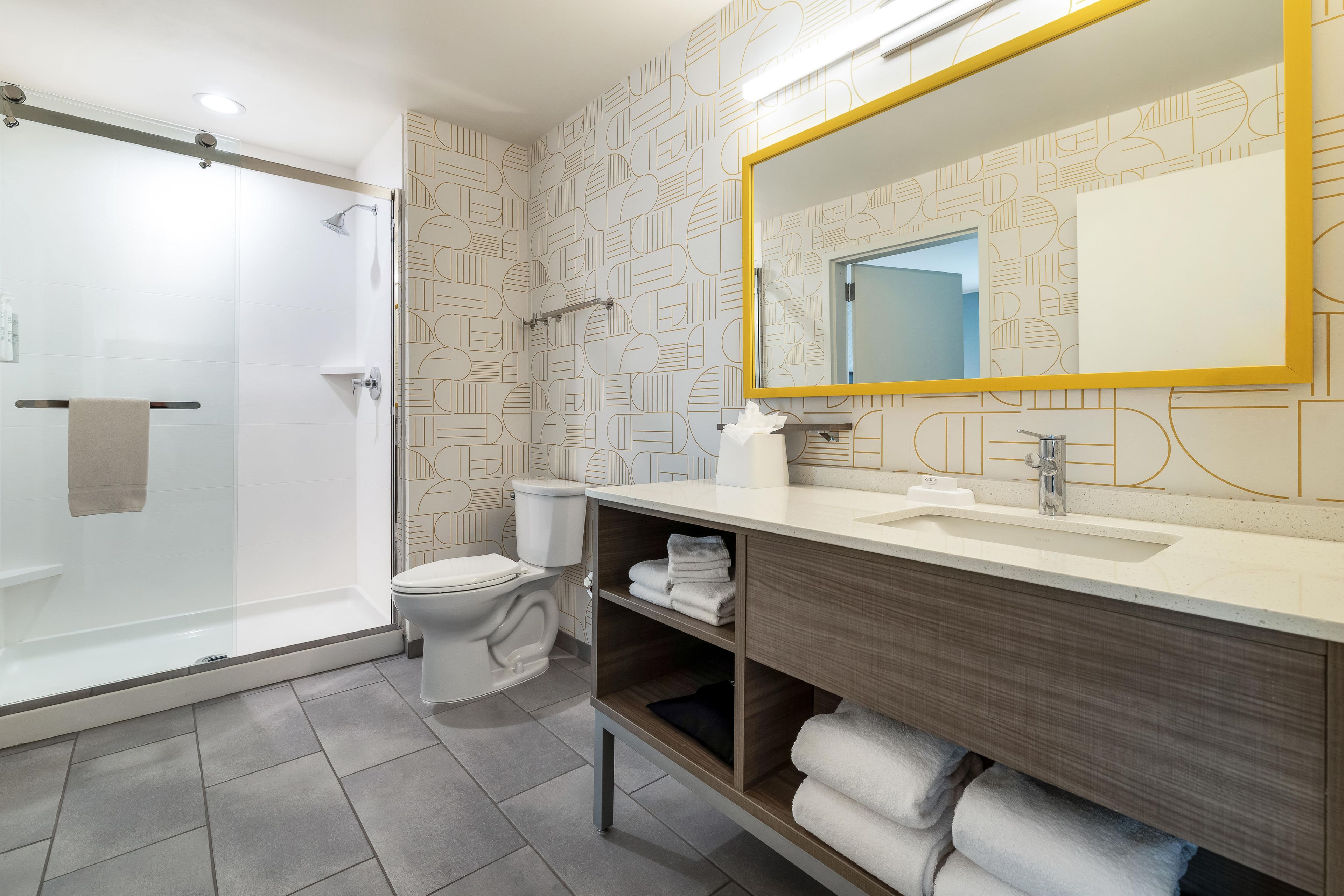 A modern bathroom with a glass shower enclosure, a toilet, a vanity with a mirror, and a towel rack.