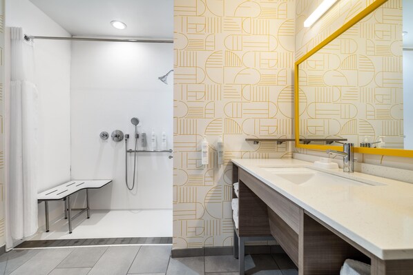 Une salle de bain moderne équipée d’une douche, d’un meuble-lavabo avec miroir et d’articles de toilette.