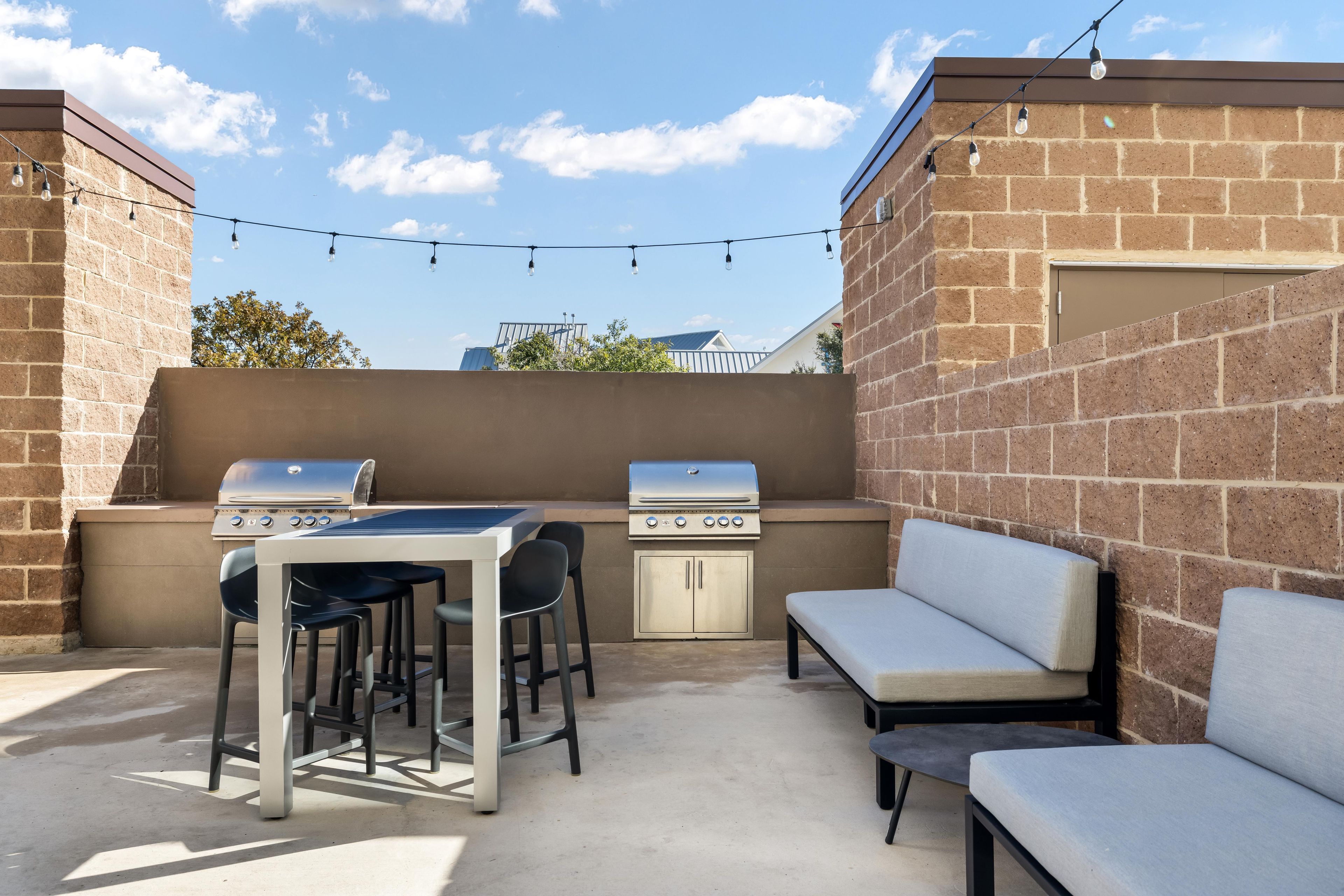An outdoor patio with two barbecue grills, a table with chairs, and a cushioned bench.