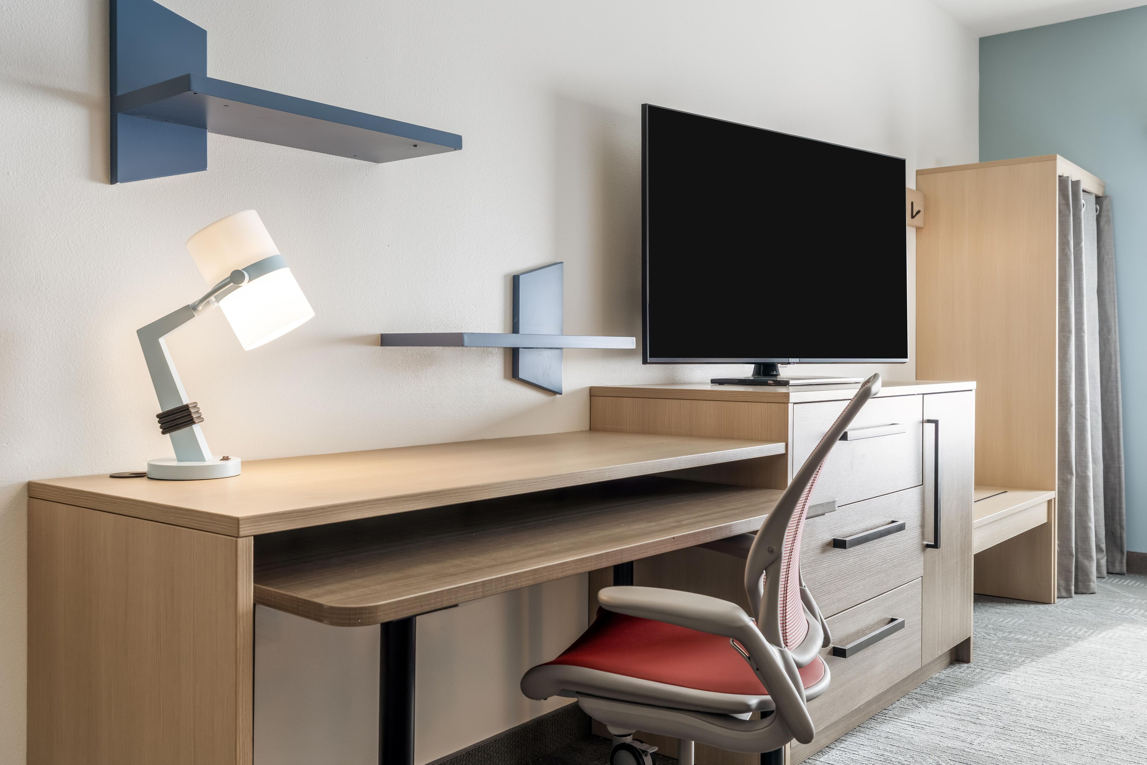 A modern office space with a desk, chair, television, and storage cabinets.