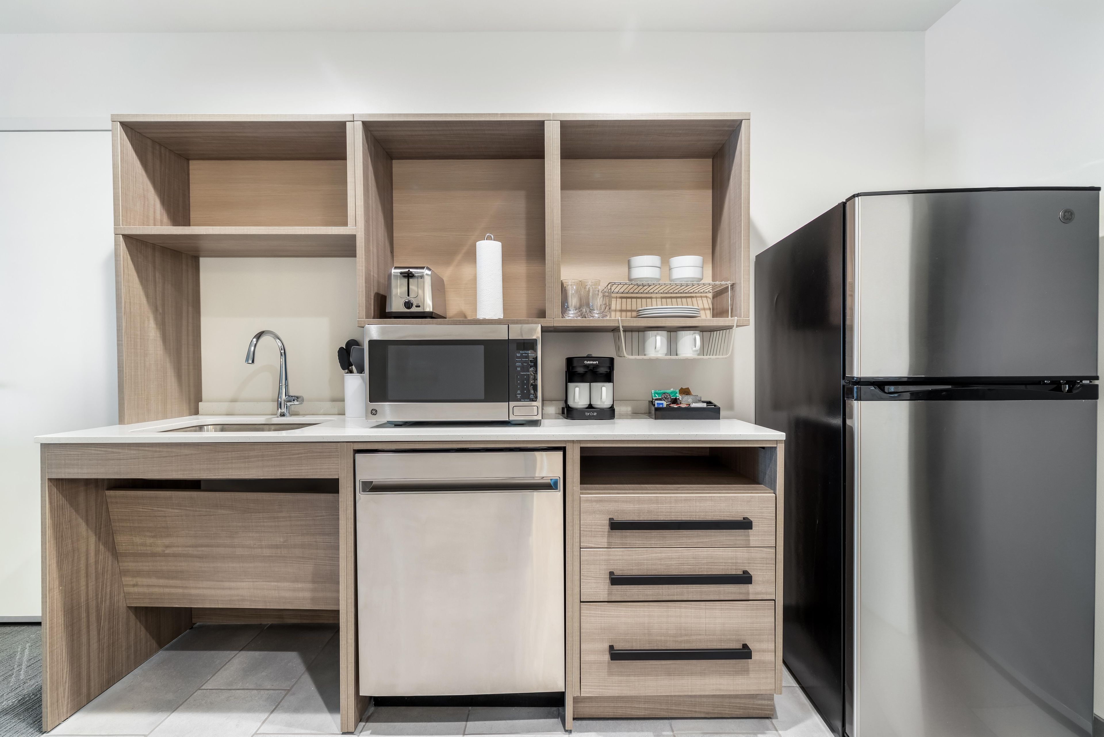 A modern kitchen with a built-in dishwasher, a stainless steel refrigerator, a microwave, and a coffee maker.