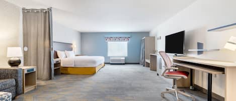 A hotel room with a bed, desk, chair, TV, and a window with curtains.