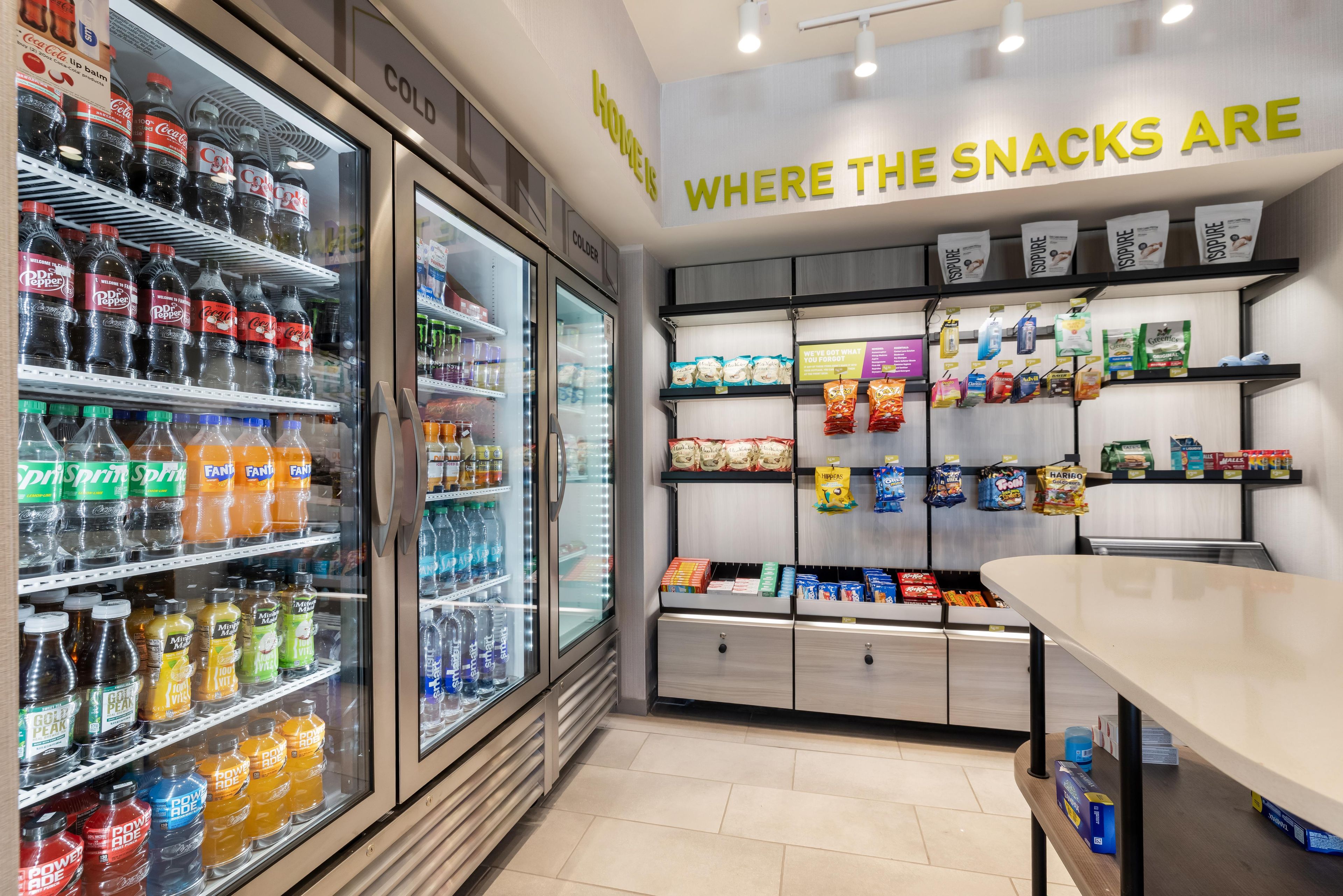 Una sección de aperitivos con estantes llenos de diferentes opciones y una zona refrigerada para bebidas.