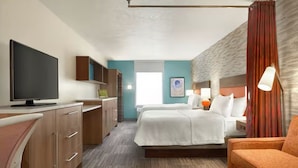 Une chambre d’hôtel comprenant un lit, un bureau avec un téléviseur à écran plat, une chaise, un canapé et une fenêtre avec des rideaux.