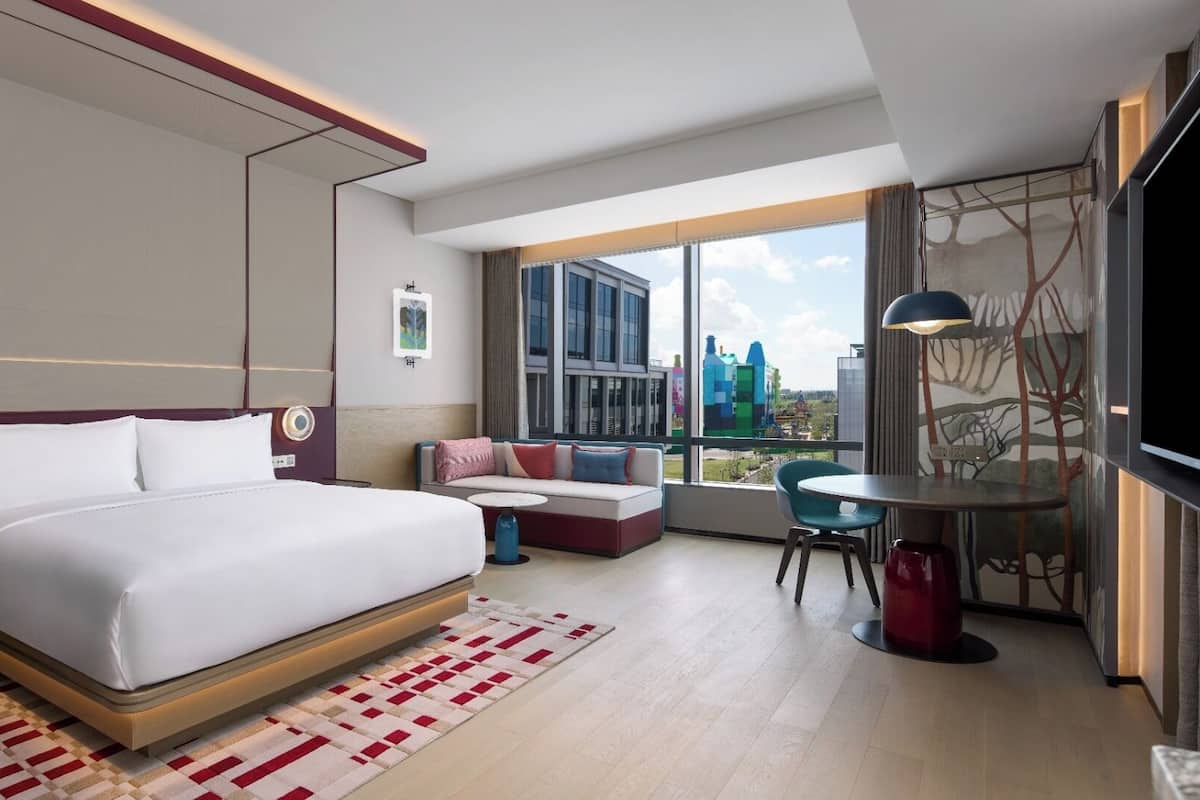 Une chambre d’hôtel moderne dotée d’un grand lit, d’un coin salon avec un canapé et des fauteuils, d’une petite table et d’une grande fenêtre donnant sur la ville.