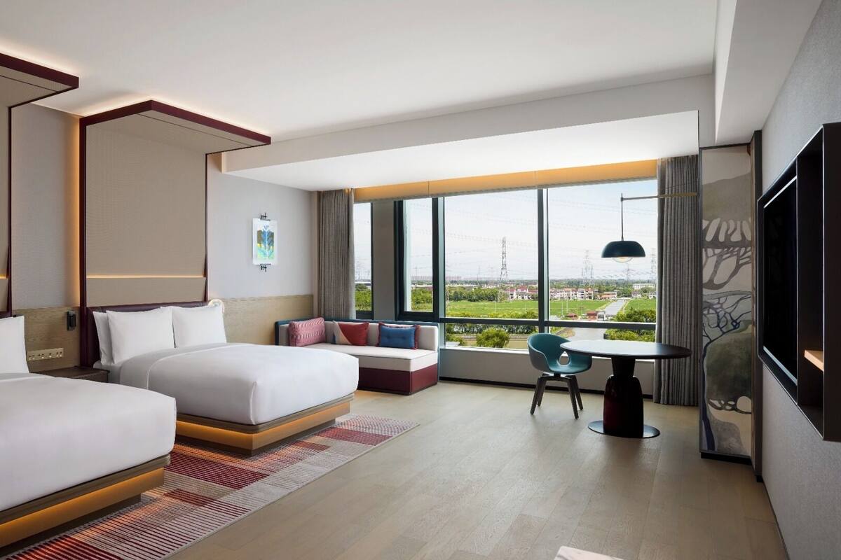 Une chambre d’hôtel moderne avec deux lits, un coin salon avec vue et une table à manger.