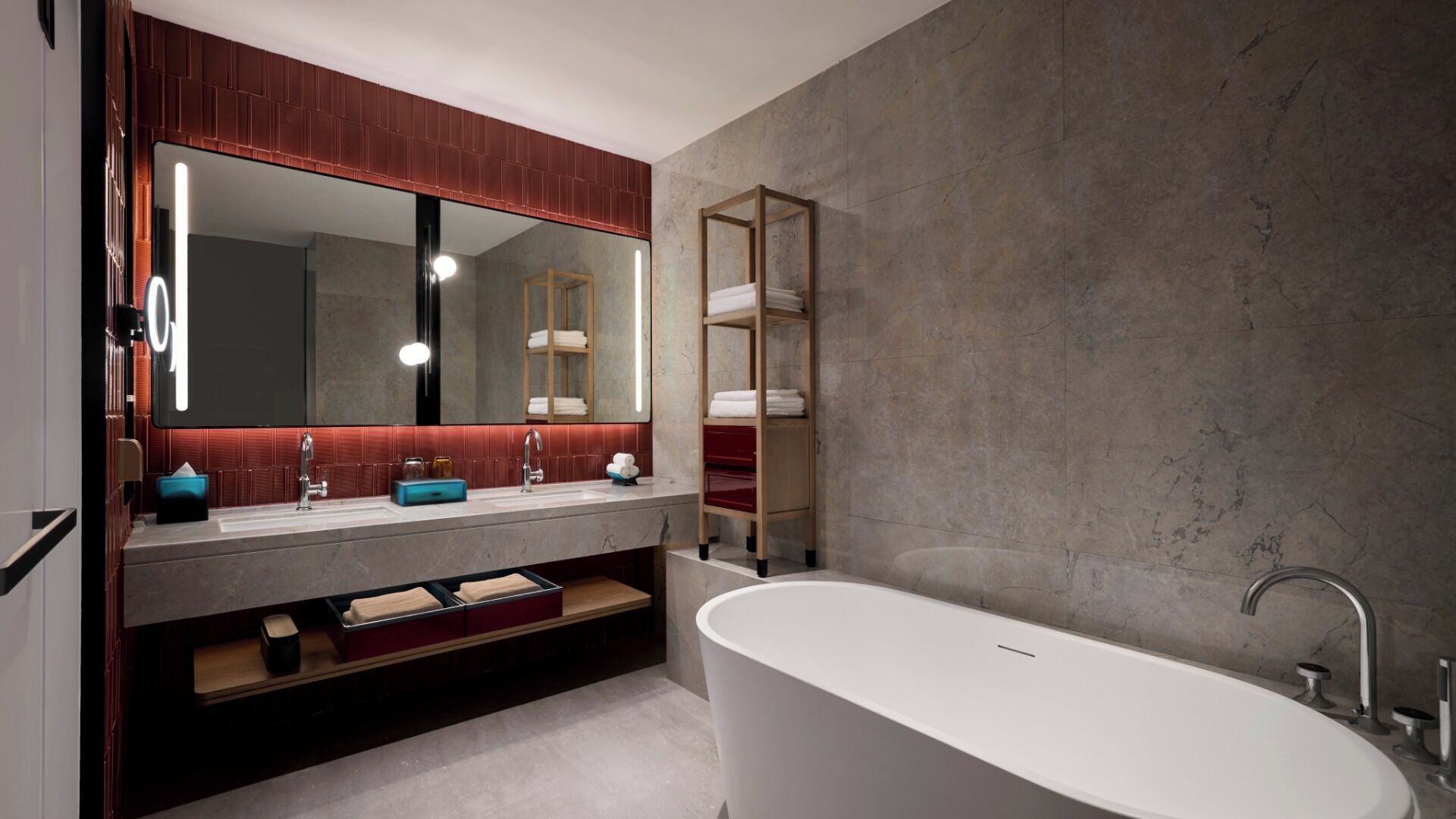 A modern bathroom with a freestanding bathtub, a large mirror, and a vanity with a red tiled backsplash.
