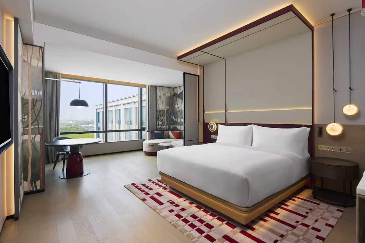 Une chambre d’hôtel moderne avec un grand lit, un bureau et une vue sur un immeuble par la fenêtre.