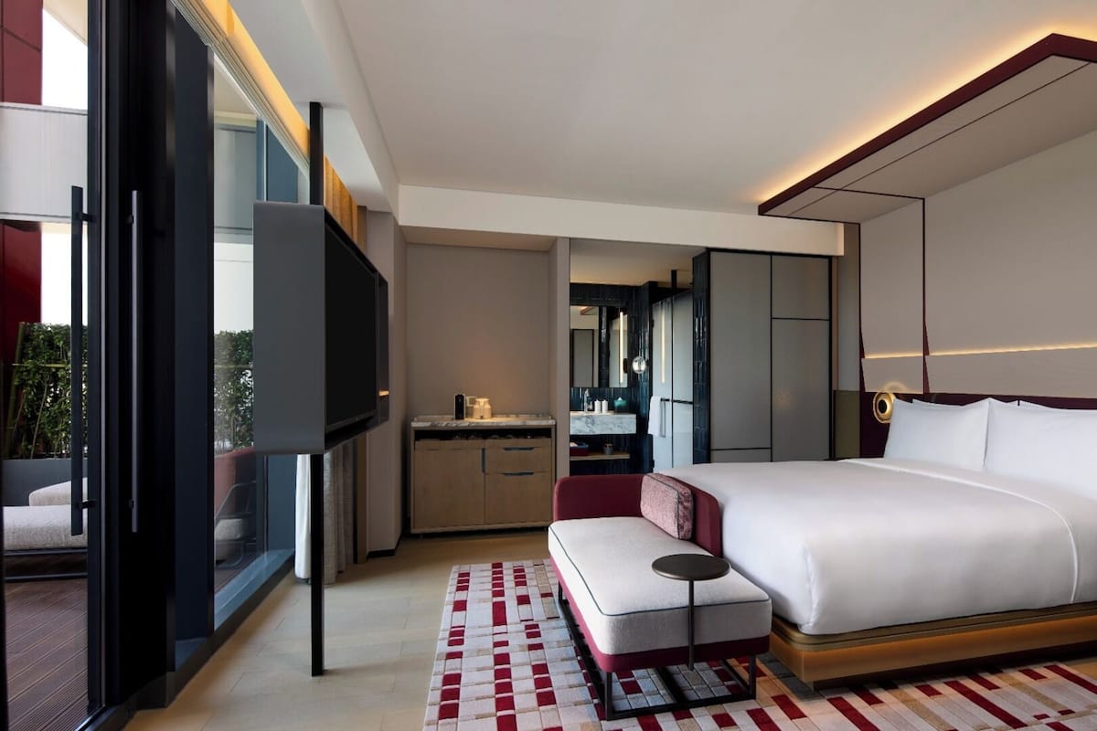 Une chambre d’hôtel moderne, dotée d’un grand lit, d’une télévision, d’un bureau et d’une salle de bain visible à travers une porte ouverte.