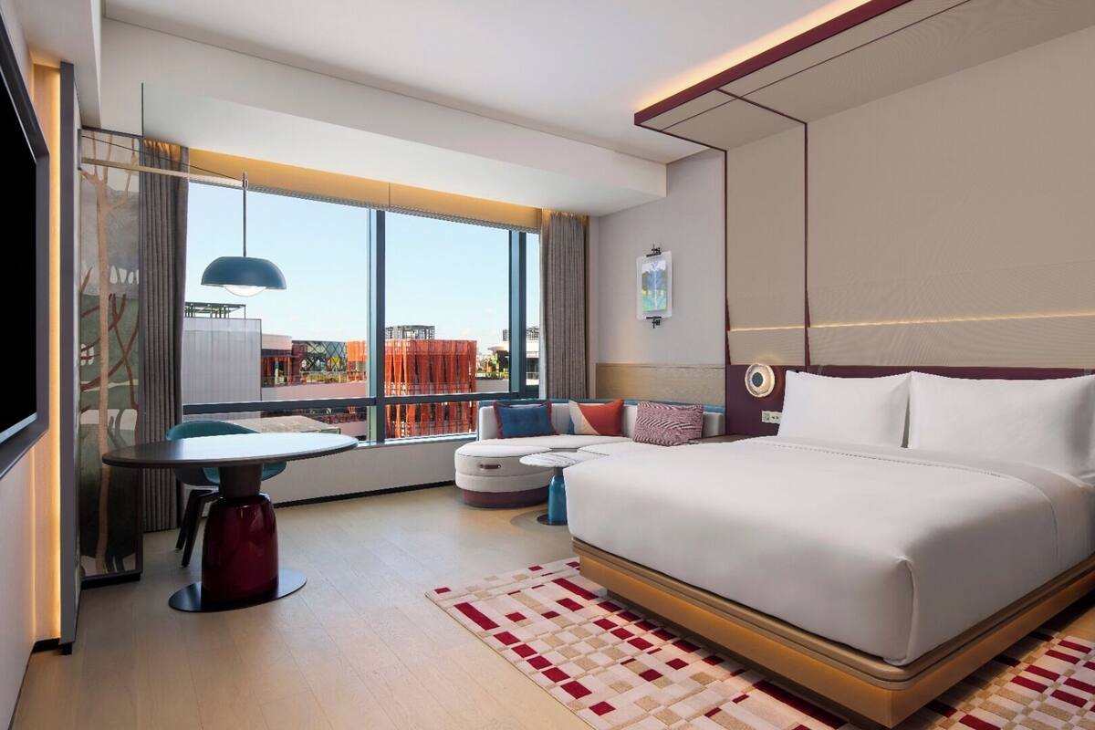 Une chambre d’hôtel moderne dotée d’un grand lit, d’un coin salon et offrant une vue sur le paysage urbain.