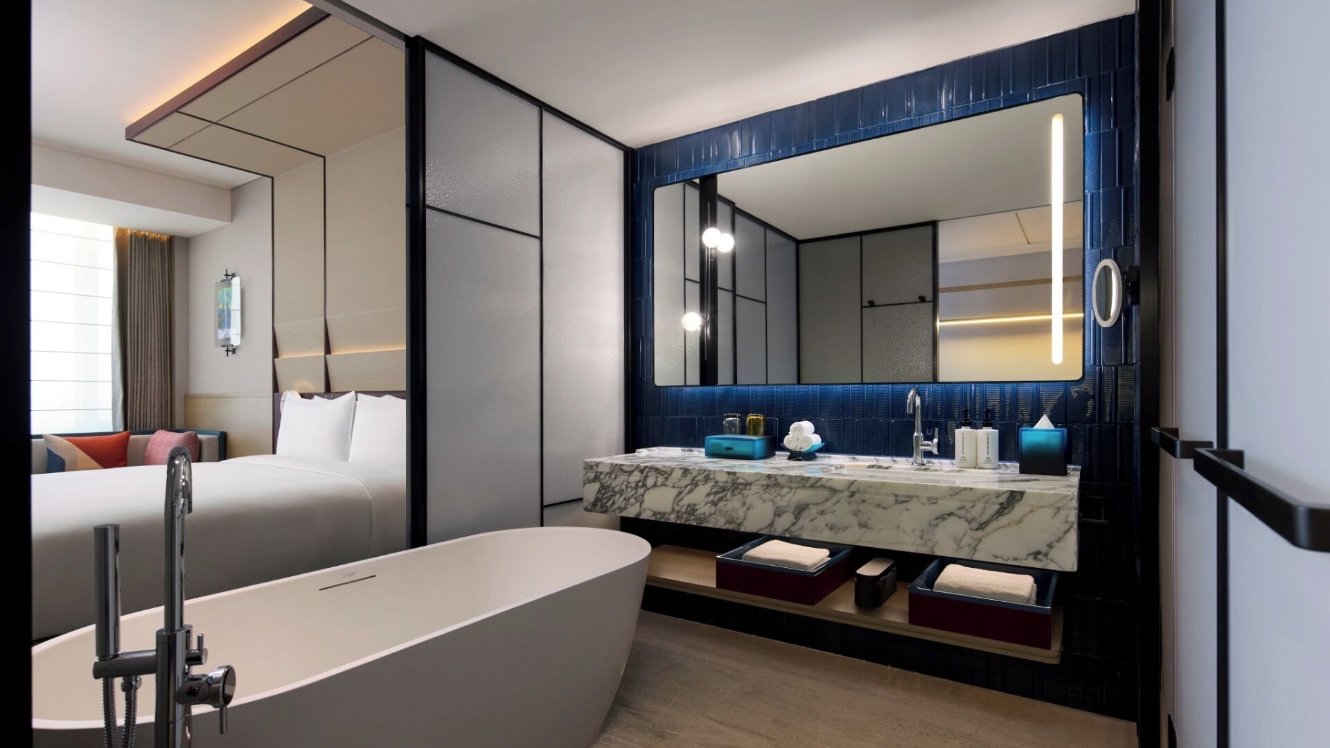 A modern hotel bathroom with a large bathtub, a marble vanity, and a large mirror.