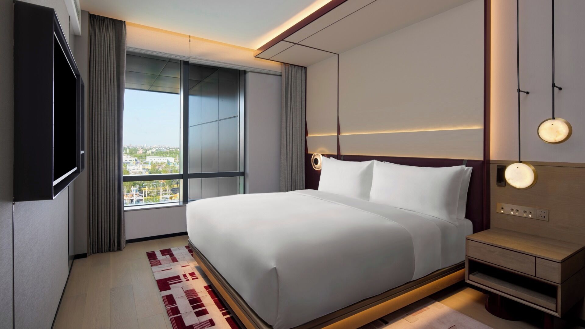 A modern hotel room with a large bed, a TV mounted on the wall, and a view of the city through the window.